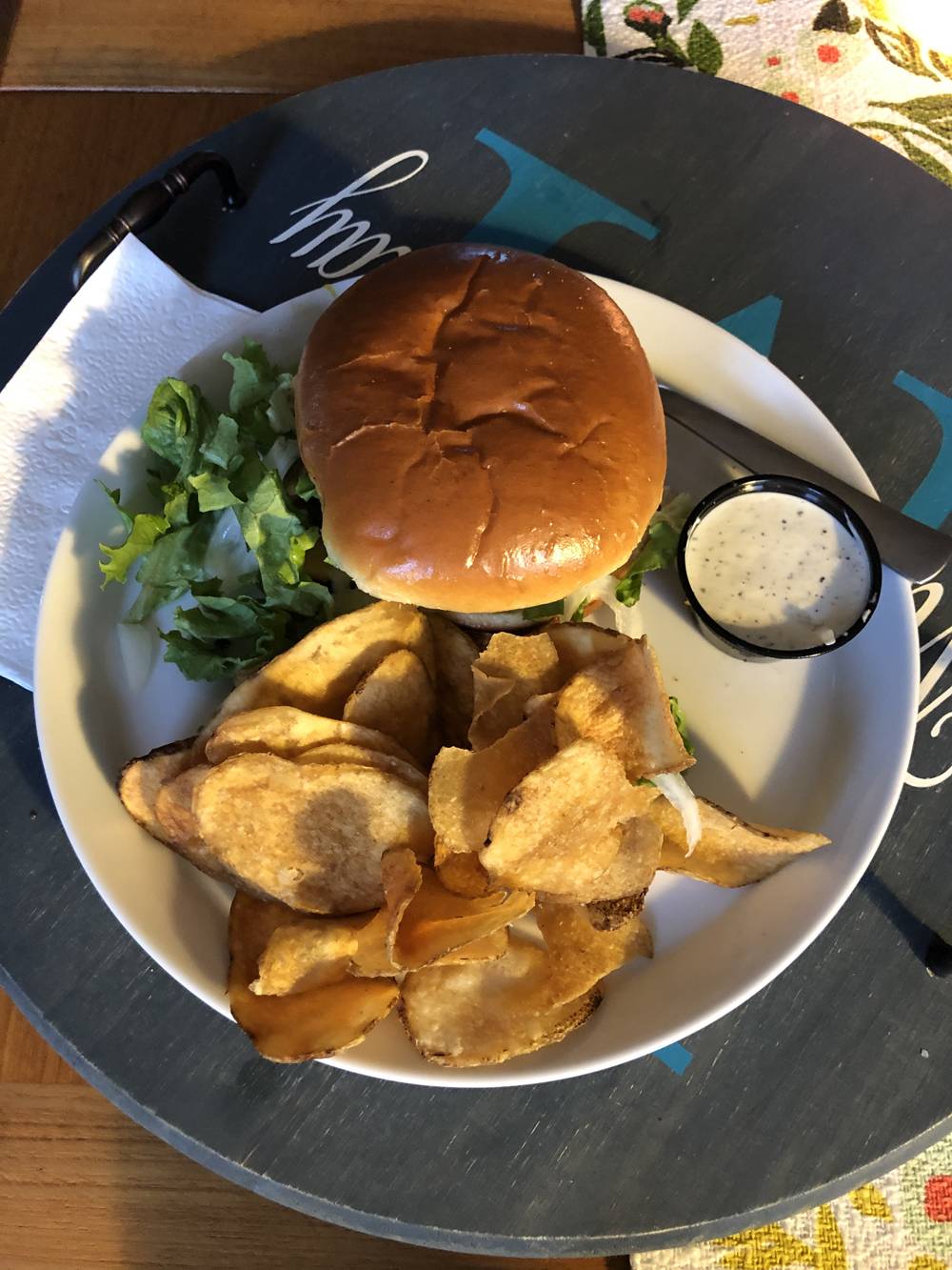 A large sandwich with shredded lettuce coming out of the sides is on a plate with potato chips and a small container of a white dipping sauce. Photo by Carly McCrory-McKay. 
