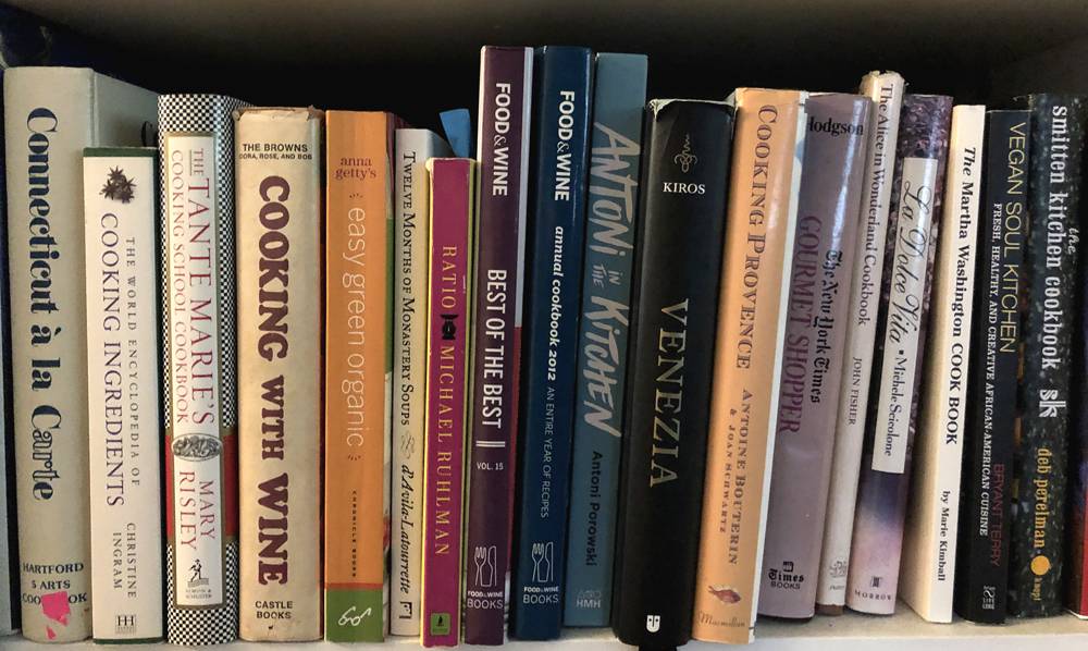 A selection of cookbooks on a white wood shelf. The cookbooks are stacked vertically. Photo by Jessica Hammie.