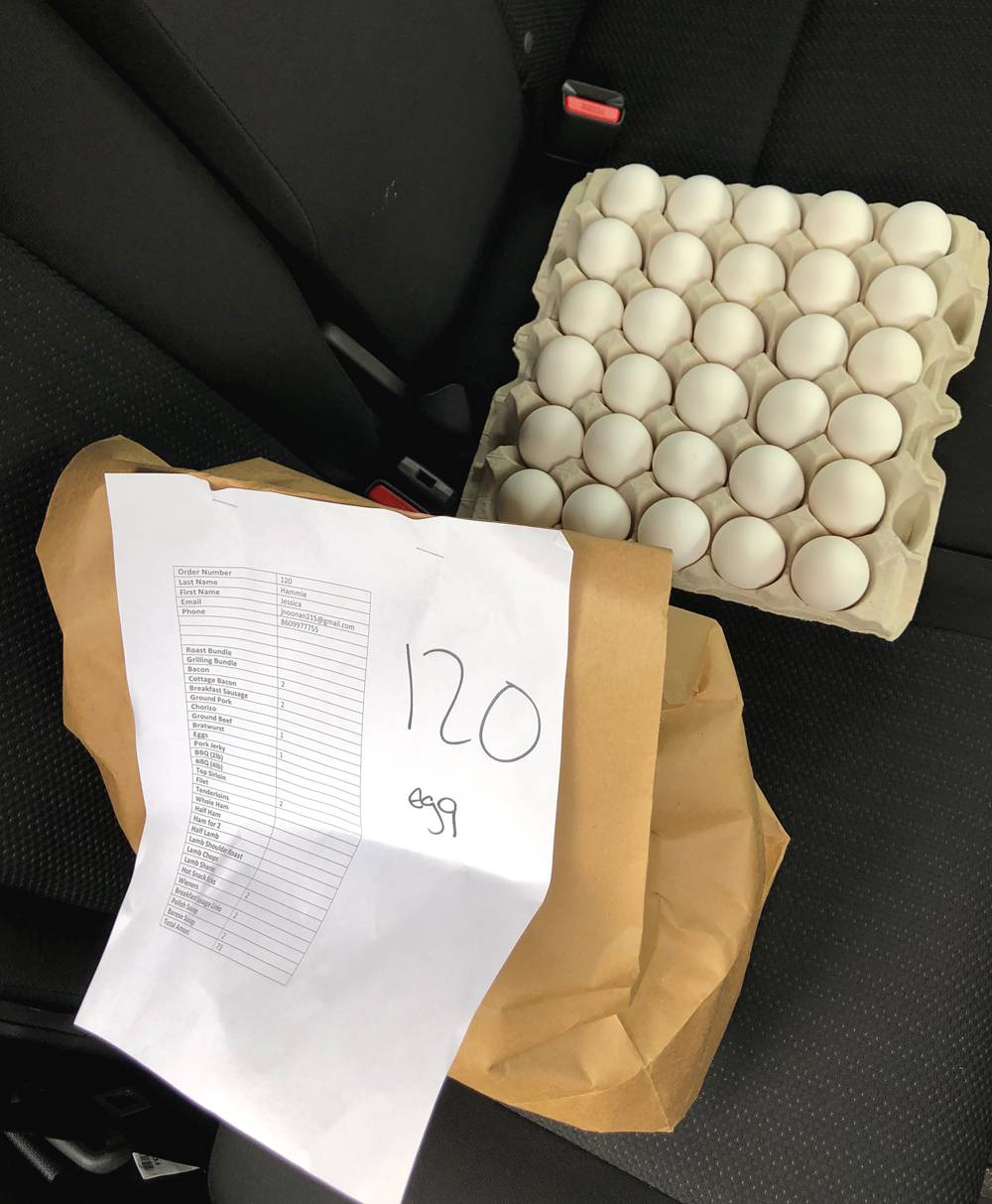 A brown paper bag with an order form stapled to it sits on the backseat of a car. There is an open carton of 30 eggs on the seat as well. Photo by Jessica Hammie. 