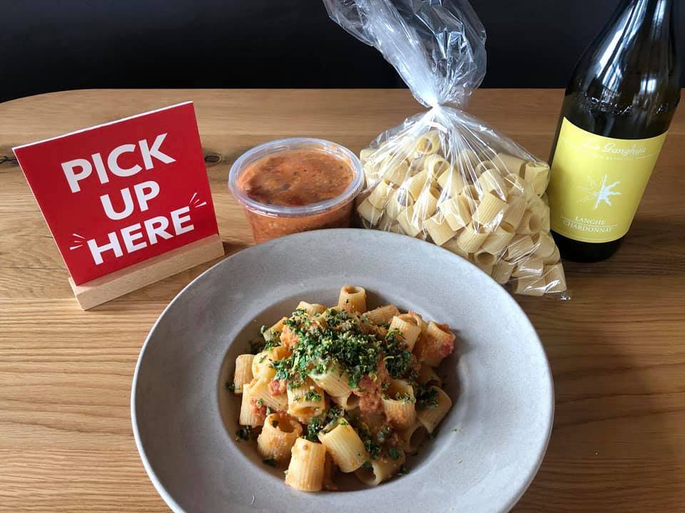 A pasta dish in a circle plate is centered in the image. The pasta is rigatoni noodles with a light sauce. A small red sign reading  