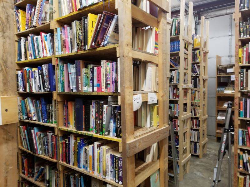 A warehouse with rows of wooden shelves and a concrete floor. The shelves are line with books. Photo from Orphans Treasure Box Facebook page.