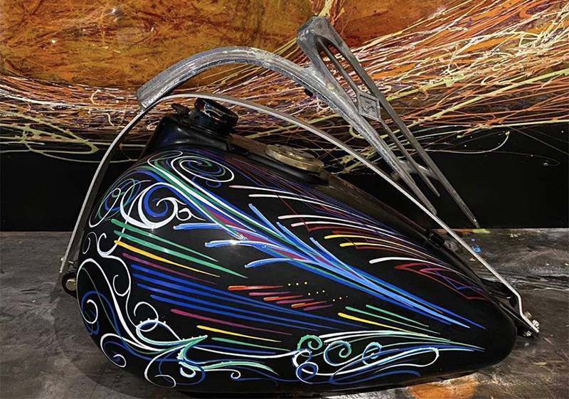 Image: Photo of black motorcycle tank painted with brightly colored lines and fluorishes. Photo from Instagram