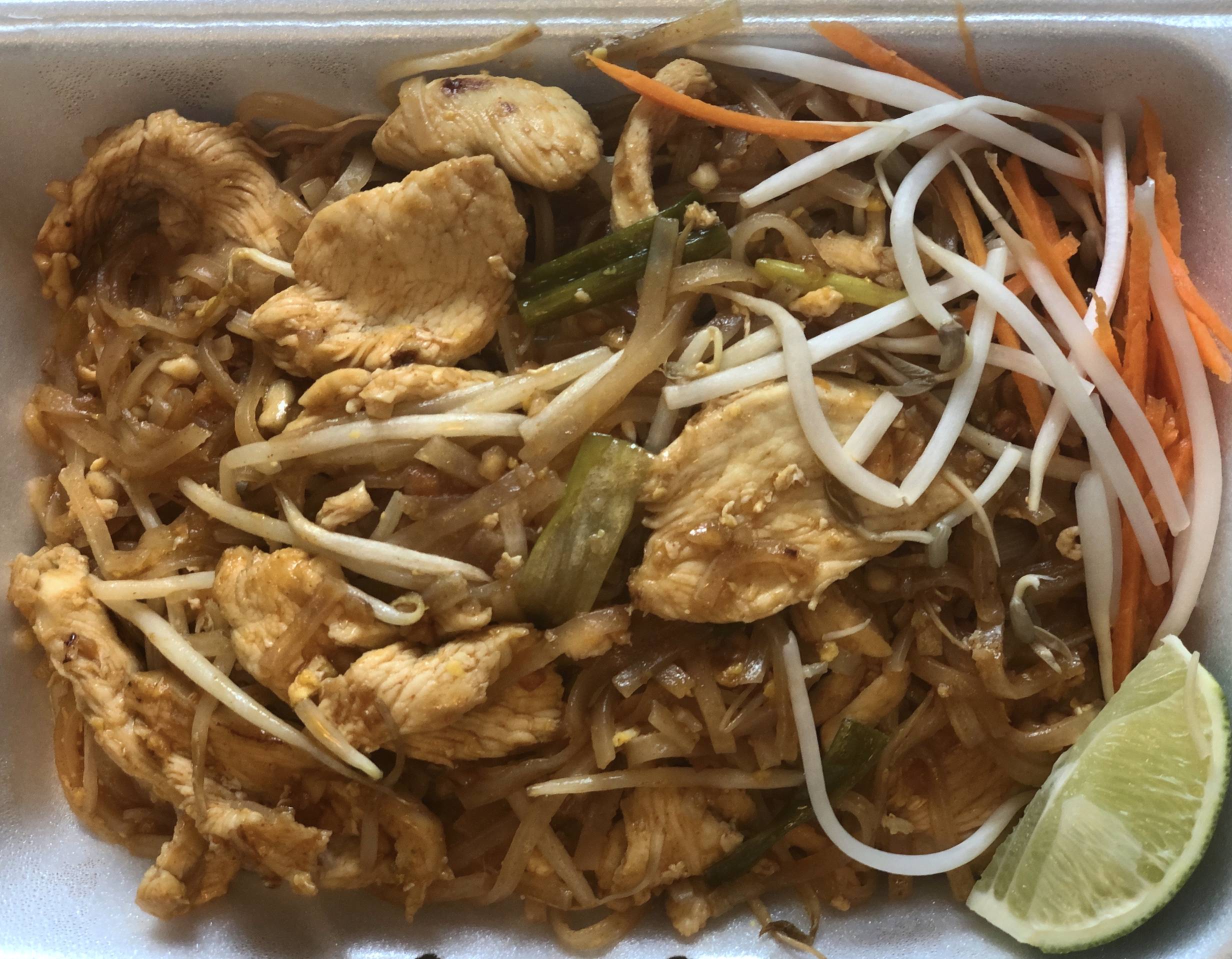 A styrofoam container of pad thai is overflowing with noodles, chicken, bean sprouts, carrots, and a lime wedge. Photo by Alyssa Buckley.