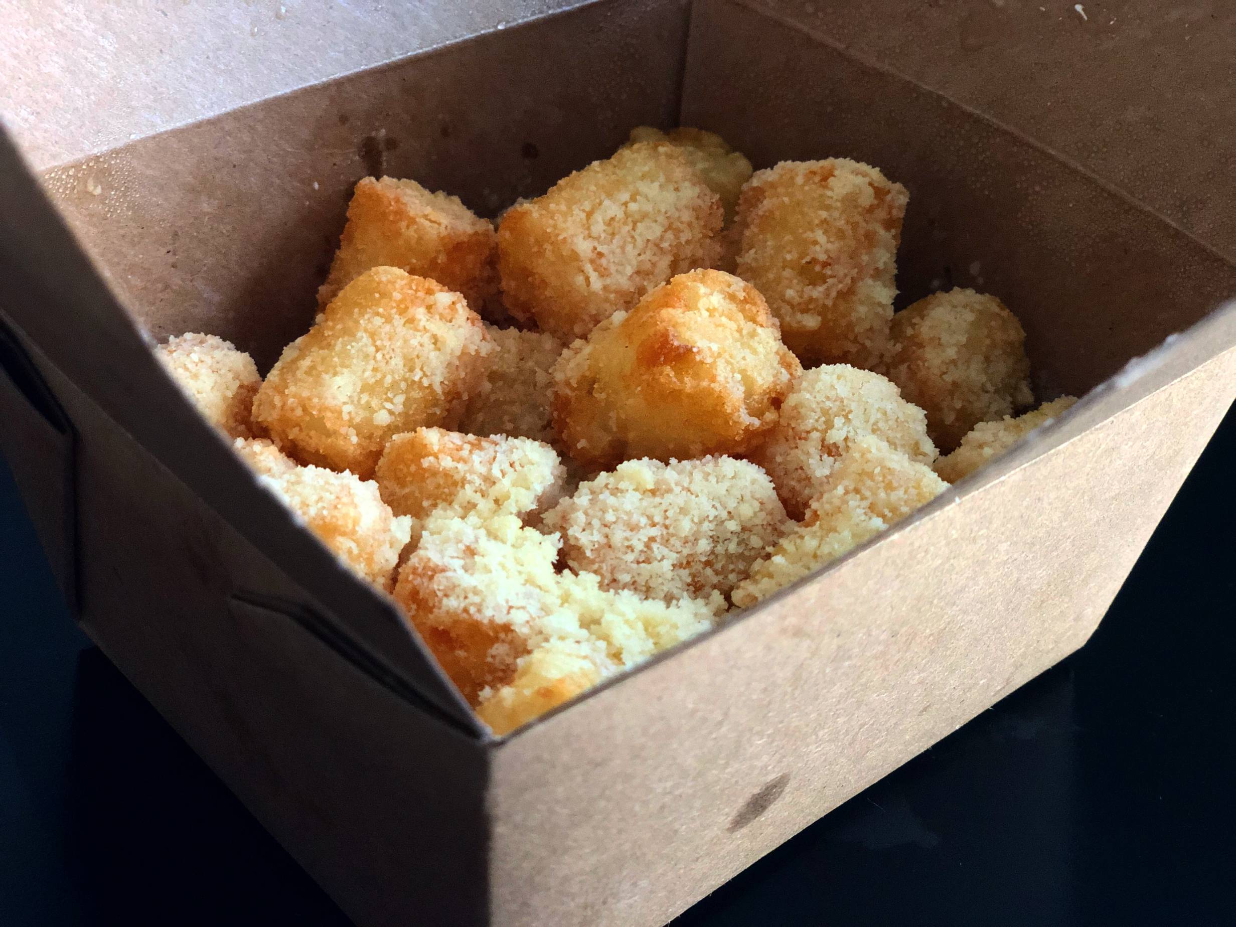 A small cardbox box is open revealing many fried tater tots covered in parmesan cheese. Photo by Alyssa Buckley.
