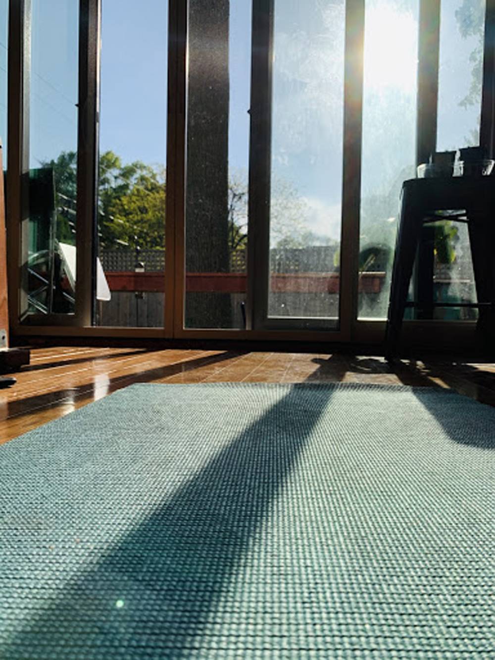 A blue yoga mat is laid out on a wood floor, looking out a wall of windows. Photo by Lindsay Aikman. 