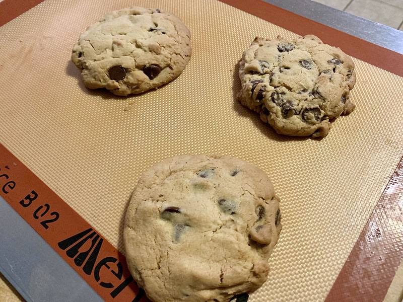 Three large chocolate chip cookies are on a baking sheet lined with a Silpat liner. Photo by Debra Domal. 