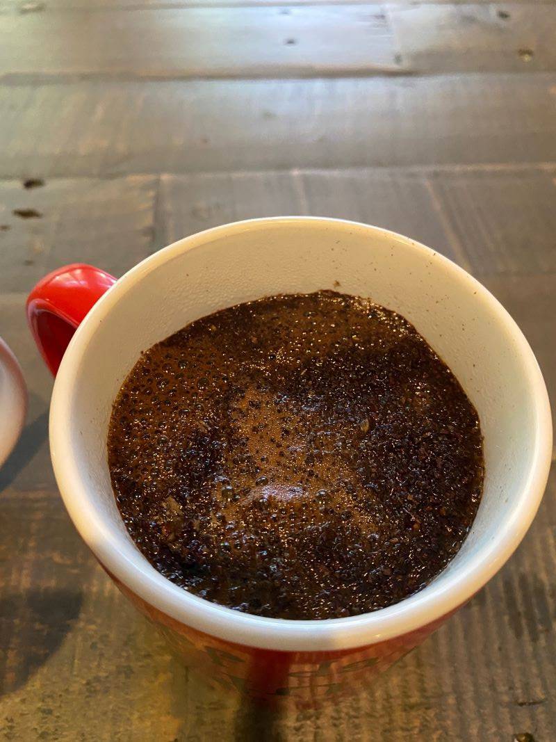 A view of the inside of a mug. The mug is white on the inside and has a red handle. It shows a crust of dark brown coffee grounds. Photo by Julie McClure.