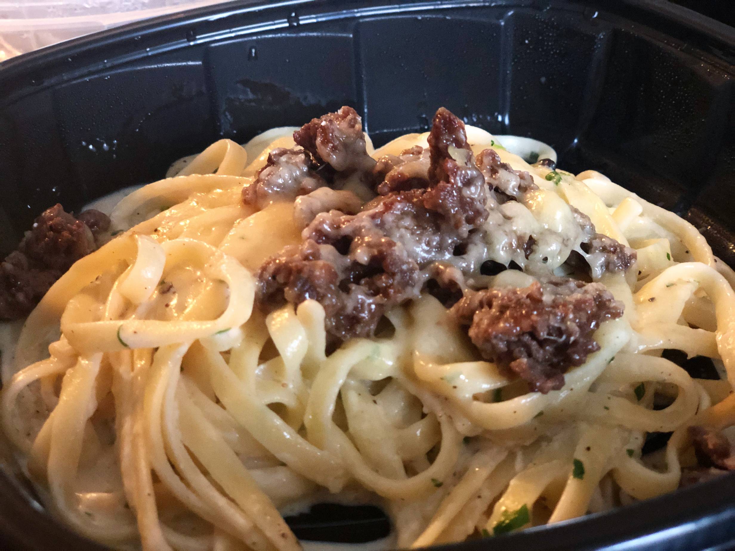 A creamy linguine dish is in a black plastic to go container. The pasta is topped with a dark meat of bulgogi beef. Photo by Alyssa Buckley.