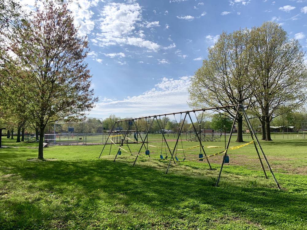 View of a park with a swing set taped off with caution tape, and an empty baseball diamond in the background. Photo by Kevin Hamilton. 