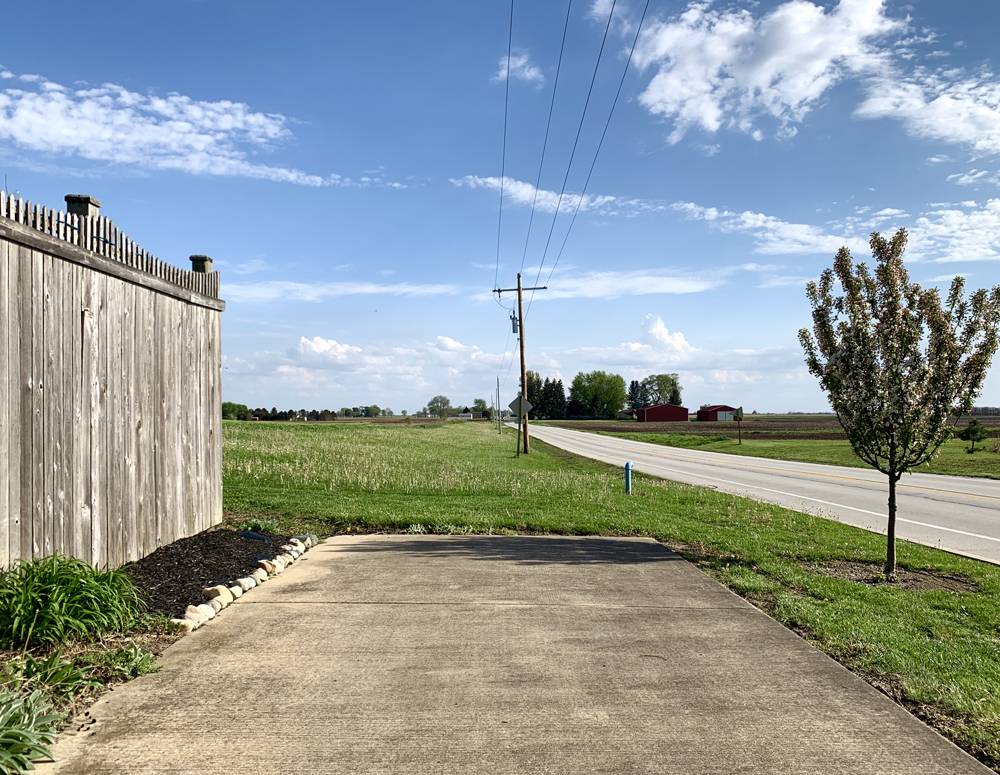A sidewalk running parallel to the road ends. There is a green field beyond it. Photo by Kevin Hamilton. 