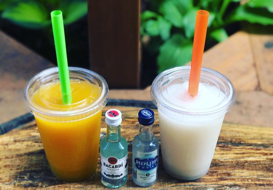 Two slushies, one orange and one white, sit on a Watson's bar in plastic cups with covers and straws. Two mini bottles of alcohol are sitting next to them. Photo from Watson's Facebook page.