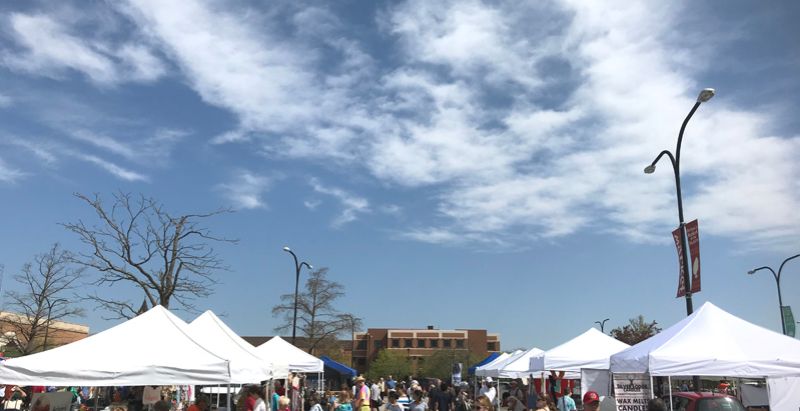 A sunny day at Urbana Market 2019. There are booths with white square tents and several people shopping. Photo by Jessica Hammie.