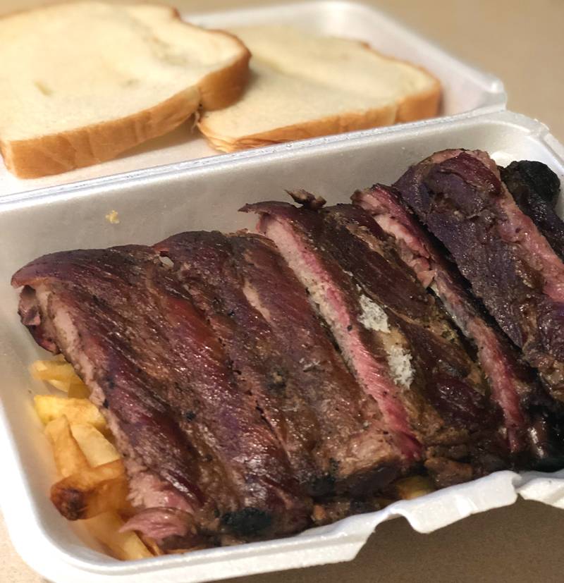 Many ribs lay lined up on top of fries in a styrofoam container. Two pieces of toast are blurred above. Photo by Jessica Hammie.