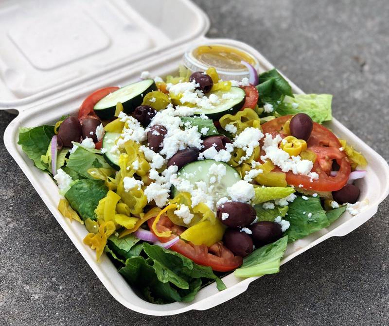 A salad fills a large styrofoam container with lettuce, feta cheese, cucumbers, and more veggies. Photo by Jessica Hammie.