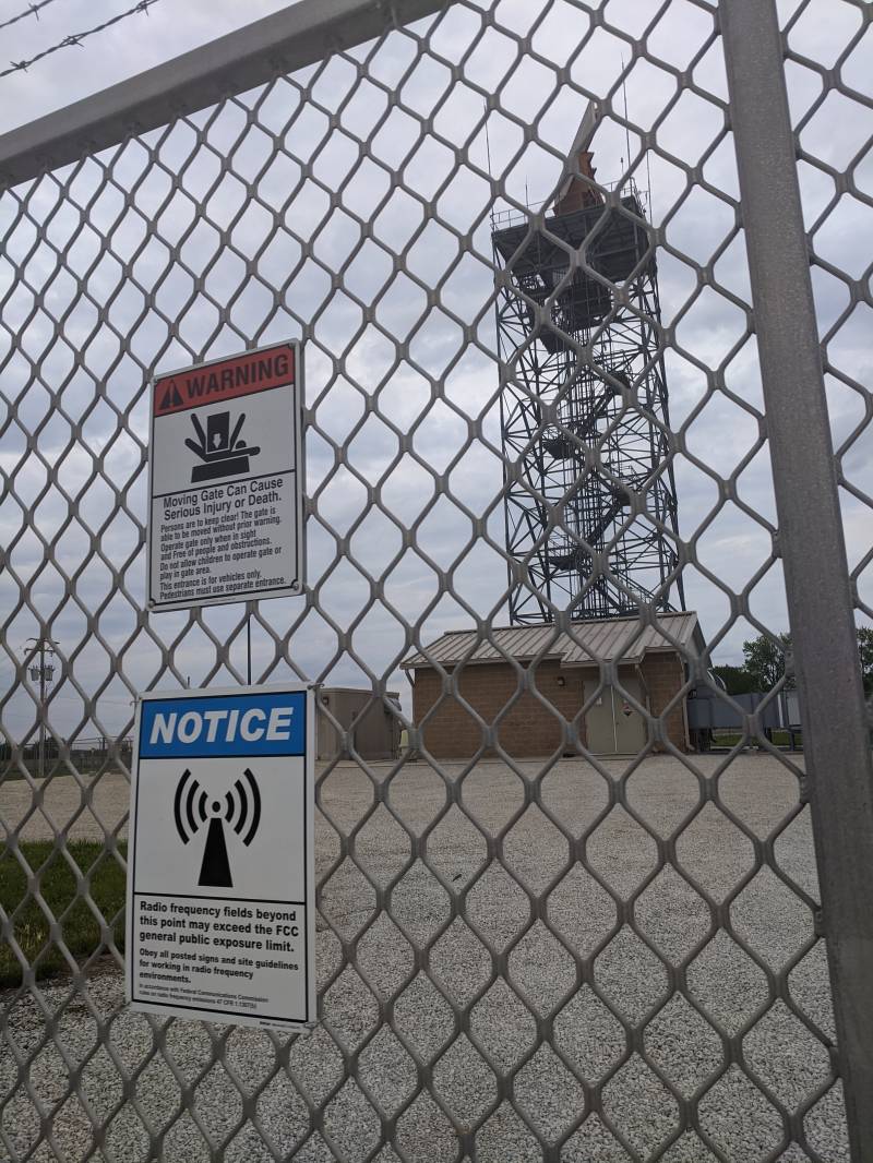 A close up of a security fence. There is a warning sign about staying away from the moving gate, and another below it that warns about radio frequency fields. Photo by Tom Ackerman.