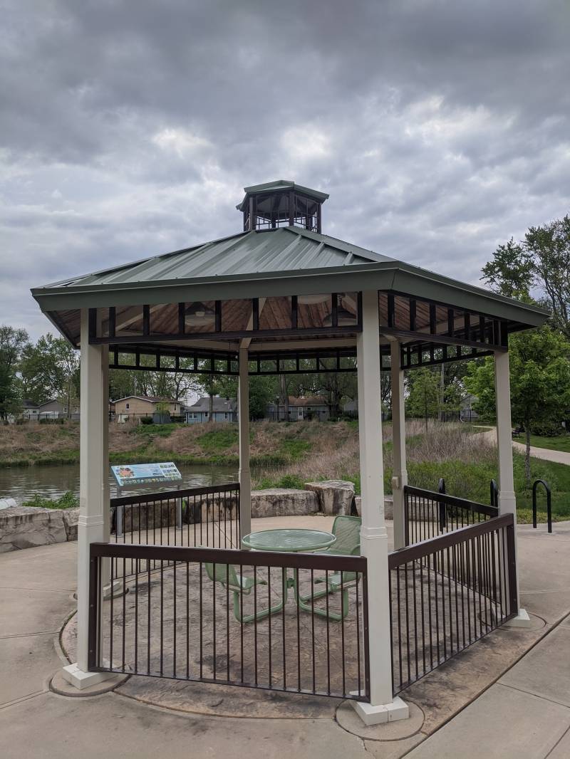 A gazebo with a green roof and ivory columns. There is a small round table with attached chairs in the center. Photo by Tom Ackerman. 