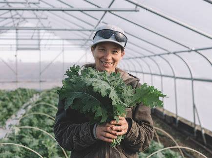 Farm co-manager Lorien Carsey holds up some fresh kale in the Blue Moon Farm greenhouse. Photo by Blue Moon Farm.