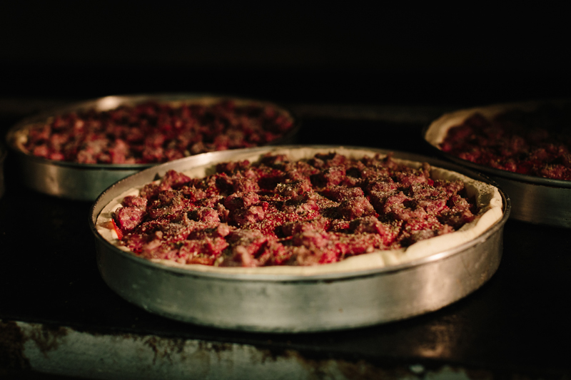 Three deep dish pizza pies with sausage on top are in a metal circle pie pans in a dark oven. Photo by Justine Bursoni.