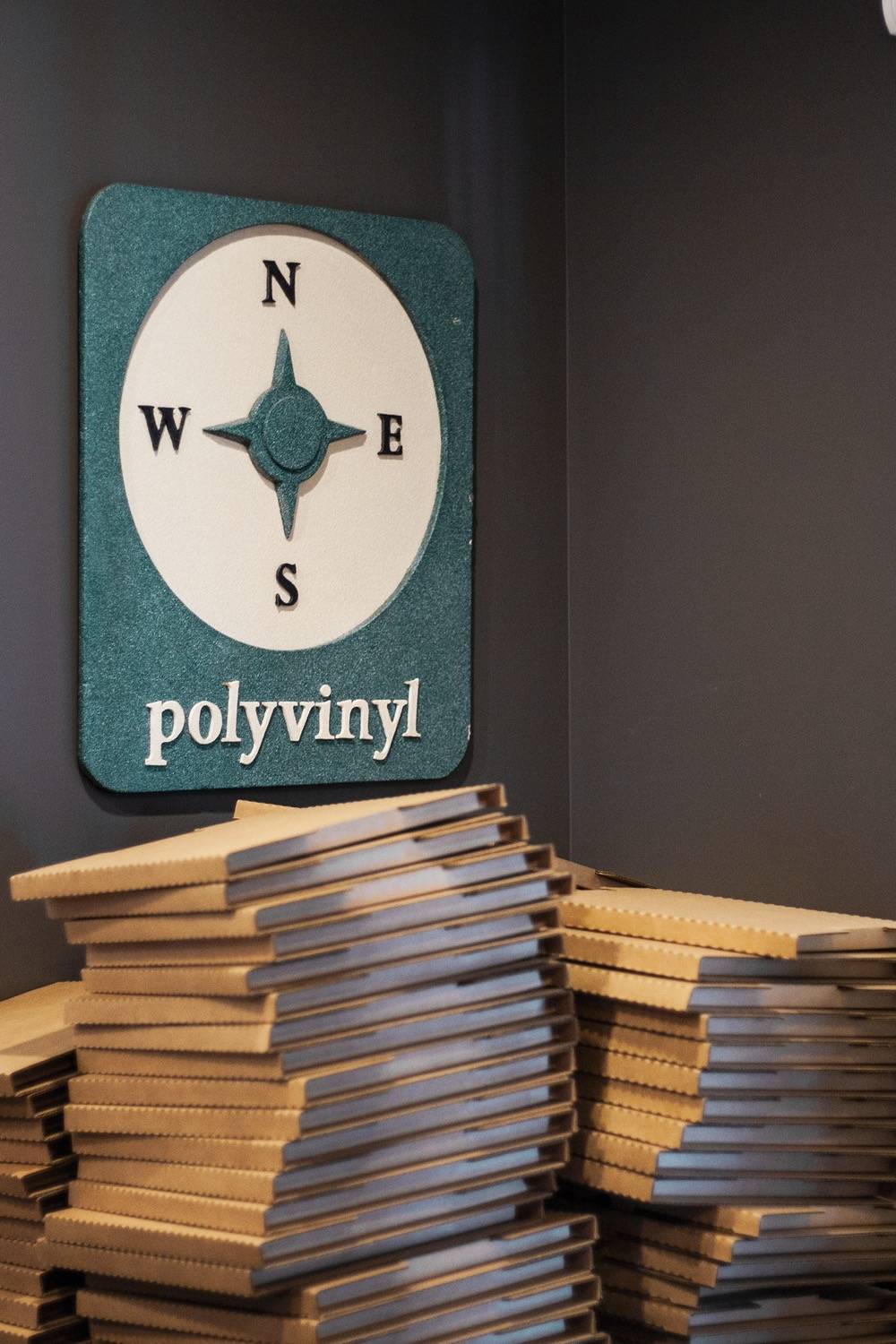 IMAGE: A green Polyvinyl sign sits above a stack of mail order cardboard boxes. Photo by Janelle Abad.