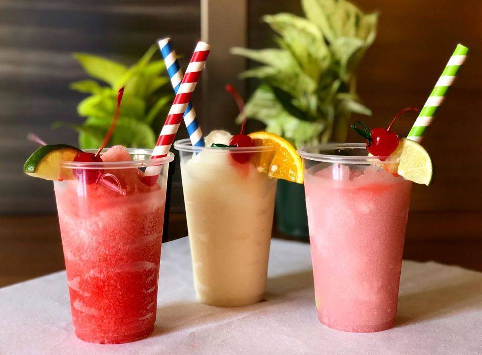Three frosty slushies sit on a bar. One is dark pink with a lime, one is light yellow with a cherry, and the third on the right is a light pink. Photo from Farren's Facebook page.