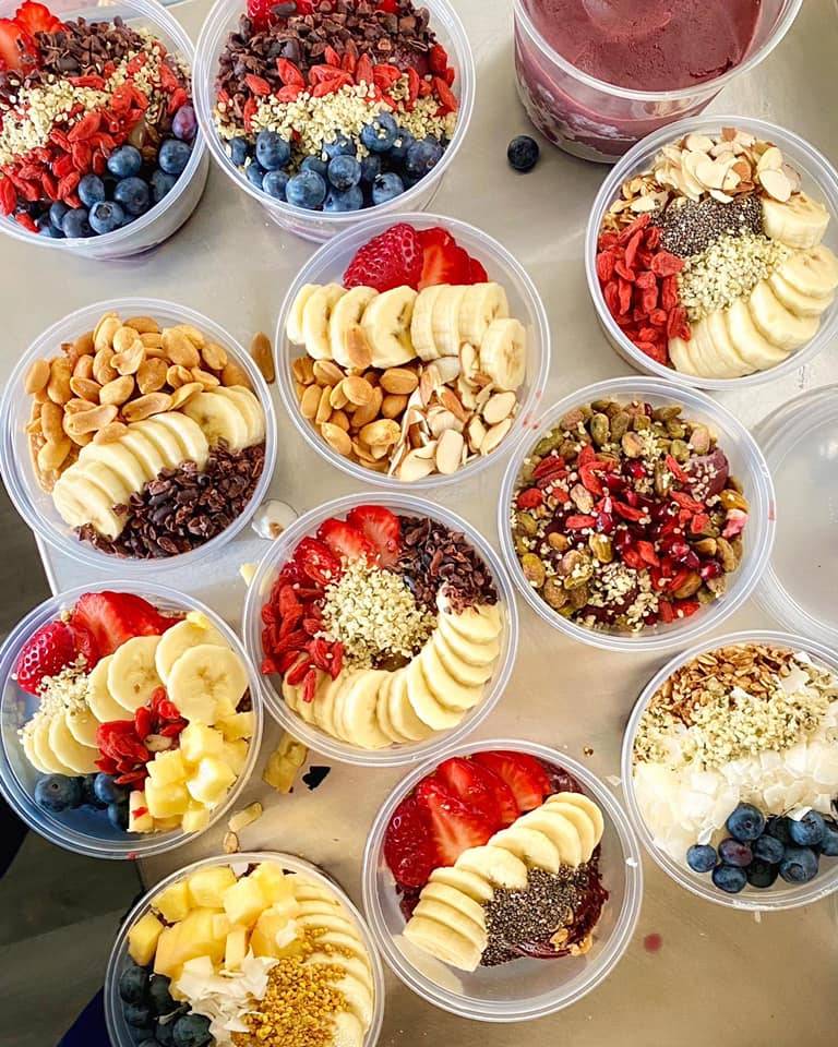 Viewed from above, several assembled acai bowls sit on a counter. Each colorful bowl is artfully topped with fruits, nuts, and other toppings. Photo by Just Bee Acai.