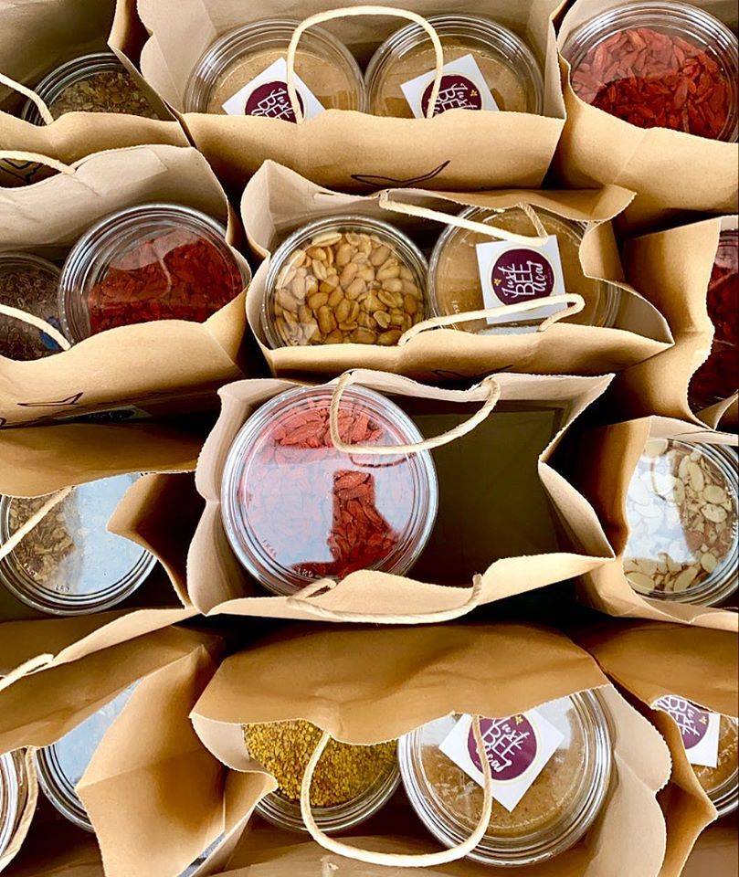 Viewed from above, several paper sacks are filled with containers of ingredients for DIY bowls. Photo by Just Bee Acai.