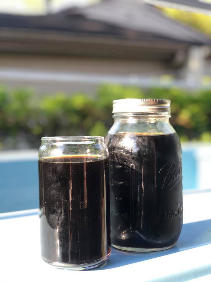 A dark cold brew coffee is in a glass cup next to a glass container of dark, cold brew coffee. Photo by NitroCup Facebook.