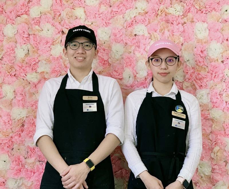 Eric Kuo and Adrianna Chung posing in front of a wall of white and pink flowers. Photo by Tasty Tart.