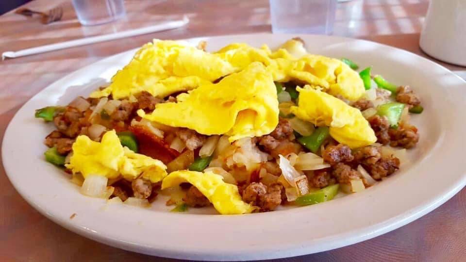 A sausage, onion, and green pepper hash is covered with scrambled eggs on a white plate. Photo by Stango Cuisine's Facebook page.