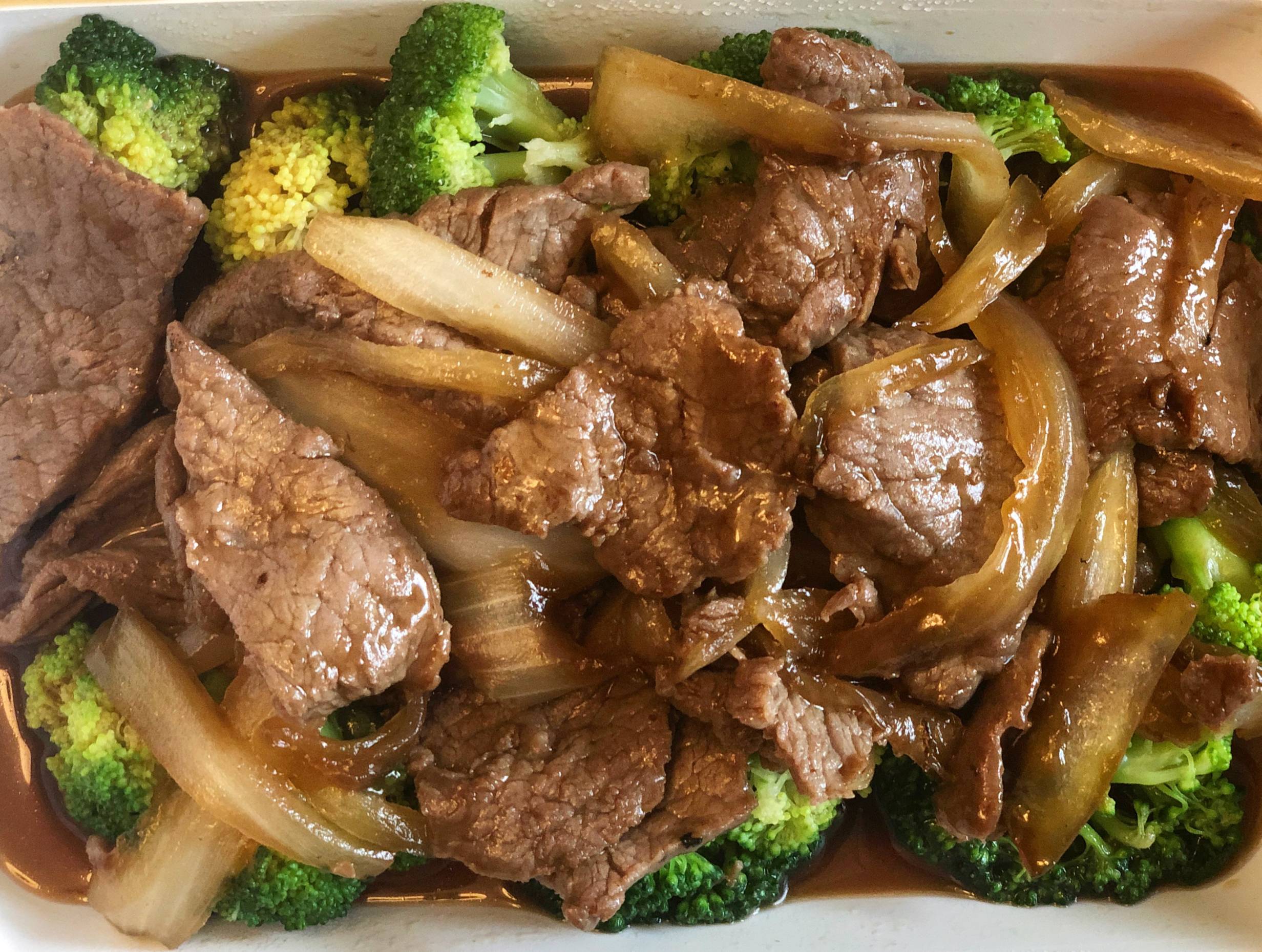 Large pieces of beef in a brown sauce with broccoli and onions are in a white plastic takeout container. This is an aerial shot. Photo by Alyssa Buckley.