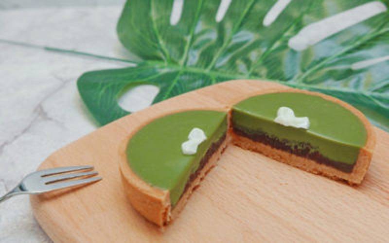 A matcha tart cut in half on a wooden cutting board with a large, tropical leave in the background. Photo by Tasty Tart.