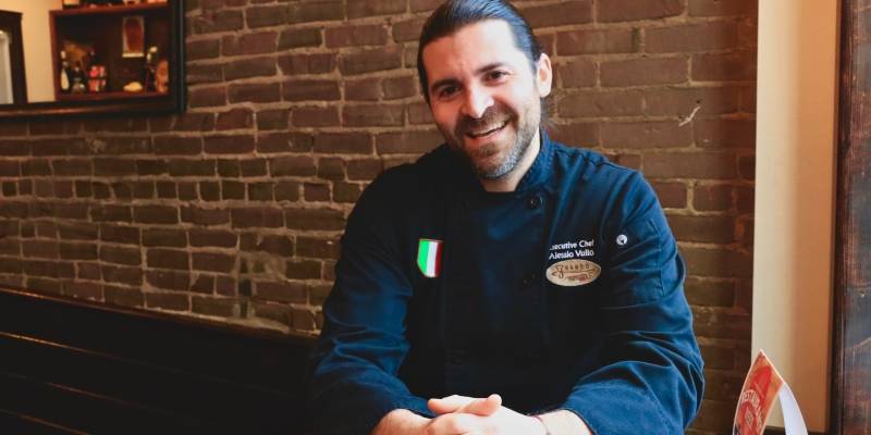A portrait of Chef Alessio Vulloin front of a red brick wall. Photo by Cara Feng.