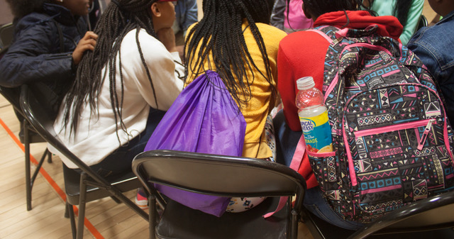 IMAGE: Three girls sit in chairs, a few of their backs. Two are wearing backpacks. Photo by Ebony Blair Smith.