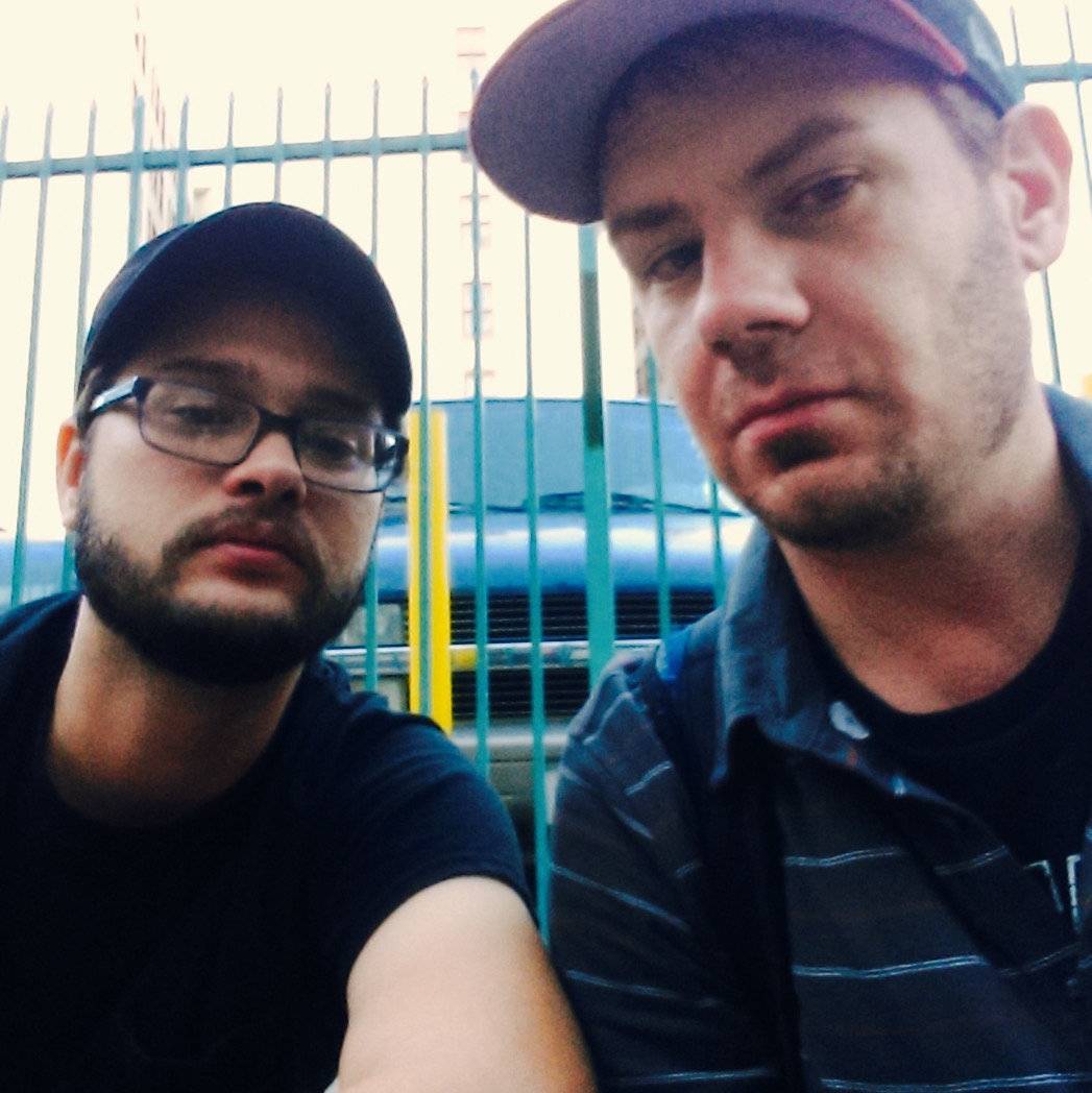 IMAGE: Two men wearing baseball caps looking at the camera. There's a fence in the background.