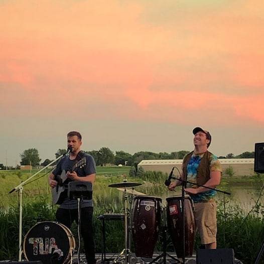 IMAGE: Two musicians playing instruments in a field. Photo from Unemployed Architects Facebook page.