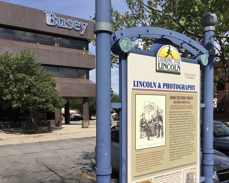 A sign with the heading Lincoln & Photography is in the foreground, with a brown rectangular building across the street. It has the word Busey in blue block letters. Photo by Rick D. Williams.