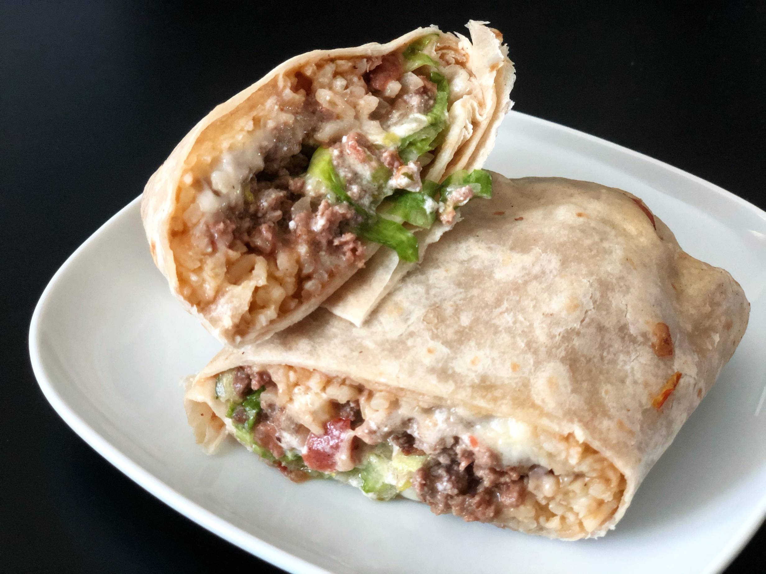 A burrito is sliced in half to reveal the inside of the burrito which is rice, ground beef, cheese, lettuce, onions, and sour cream. Photo by Alyssa Buckley.