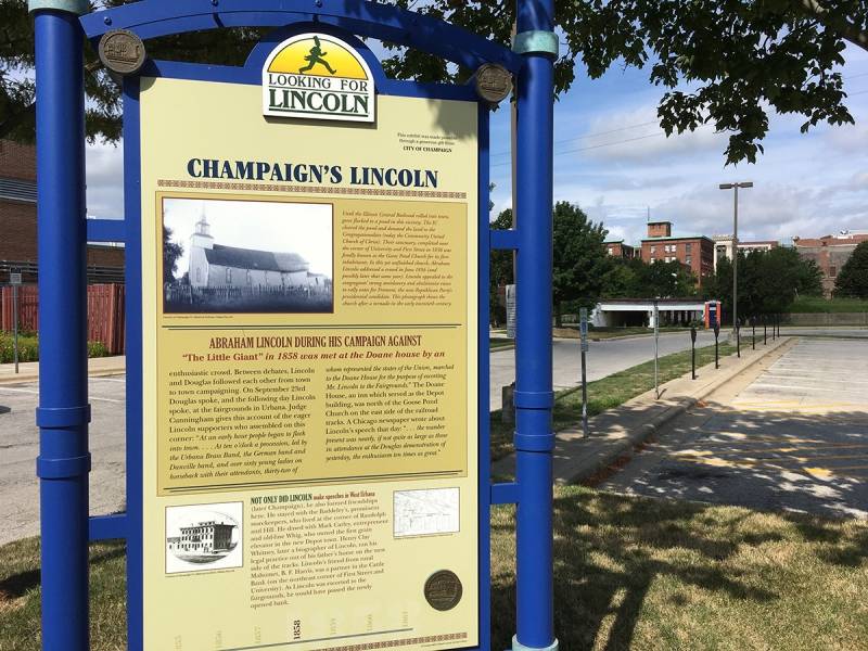 A sign with the heading Champaign's Lincoln stands in the foreground in front of a parking lot lined with parking meters. Photo by Rick D. Williams.