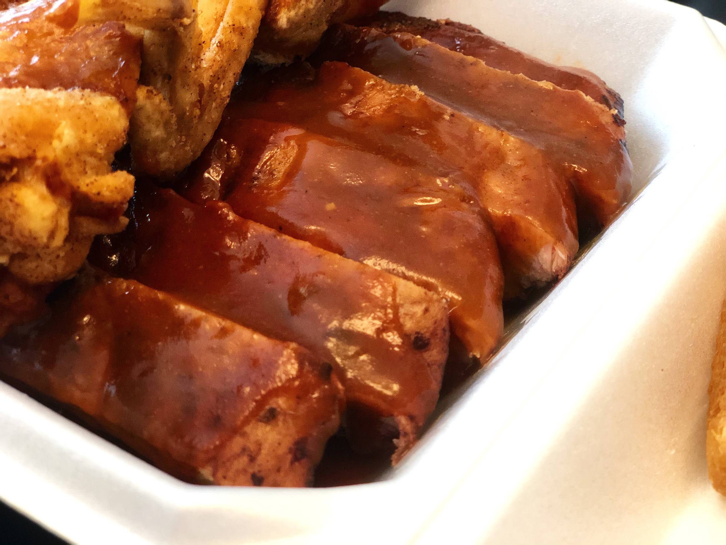 Several ribs covered in sauce sit in a white styrofoam container. Photo by Alyssa Buckley.