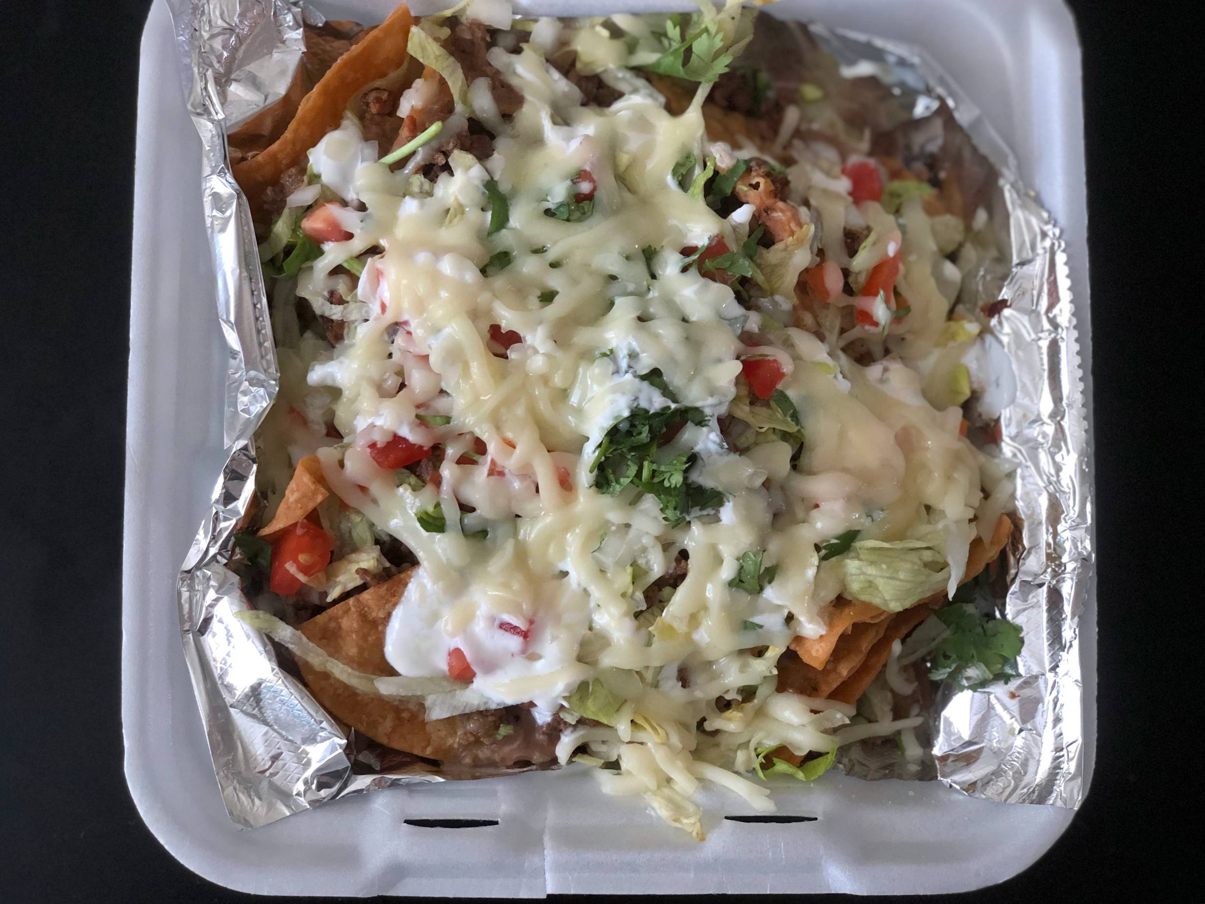 A large, square styrofoam container holds a lot of nachos covered in cheese inside. Photo by Alyssa Buckley.