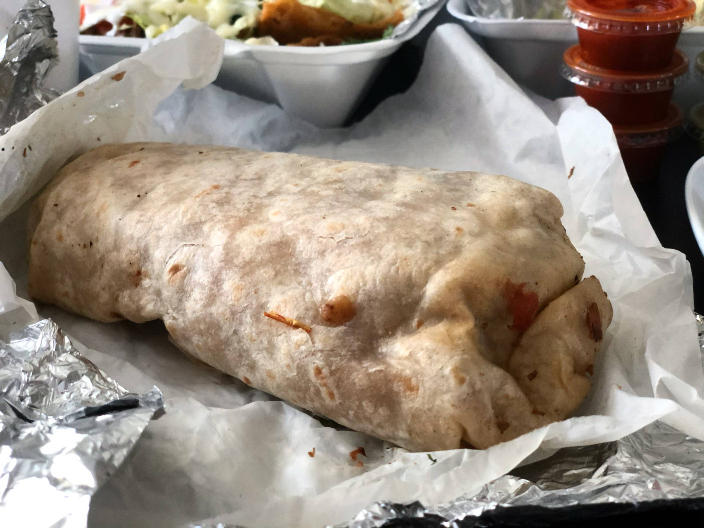 A large burrito rolled lays on a parchment paper on top of tin foil. Photo by Alyssa Buckley.