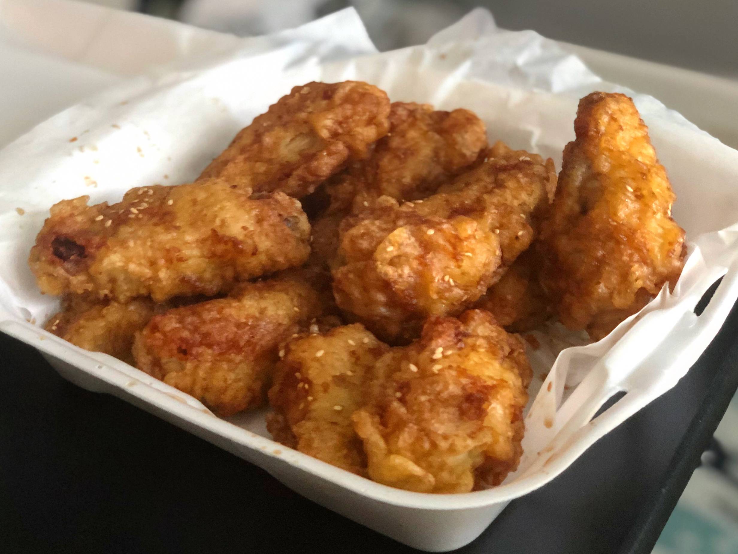 In a white styrofoam container, twelve tempura fried chicken wings with a light brown sauce are stacked high. Photo by Alyssa Buckley.