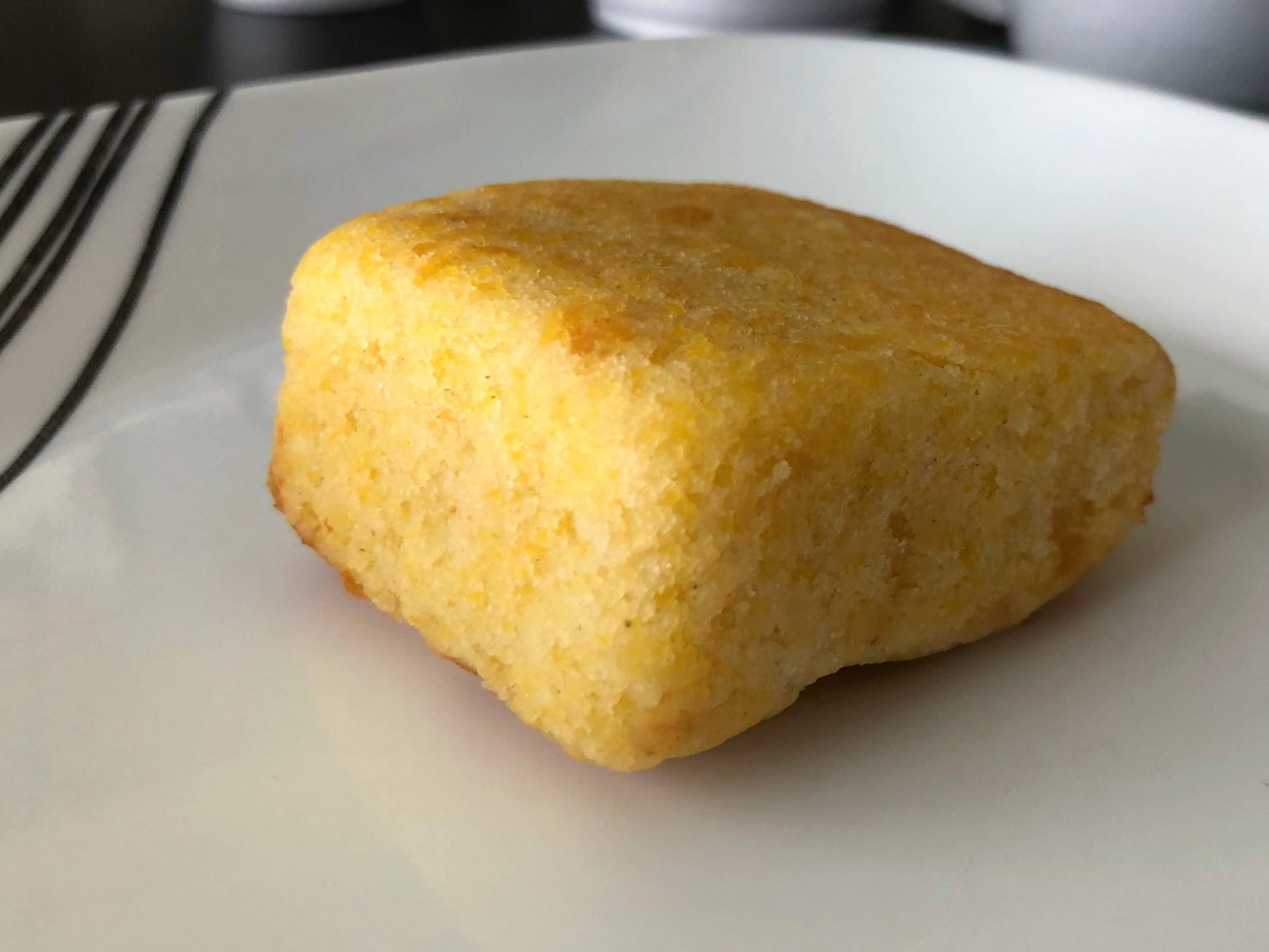 A yellow square of cornbread is on a white plate on a black table. Photo by Alyssa Buckley.