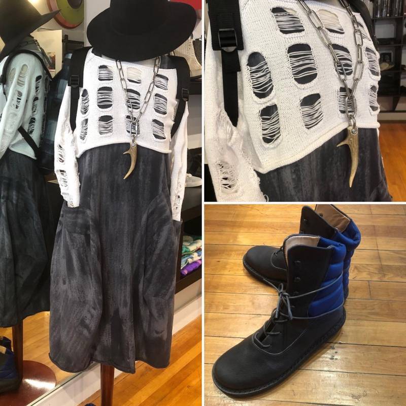 Three images: A full length image of a mannequin wearing a white sweater with holes cut out over a gray dress. A black hat sits on top, and a linked necklace with large bone like pendant is draped over it. There is also a close up photo of the top half, and a close up photo of a pair of black and dark blue ankle boots. Image from Circles Instagram. 