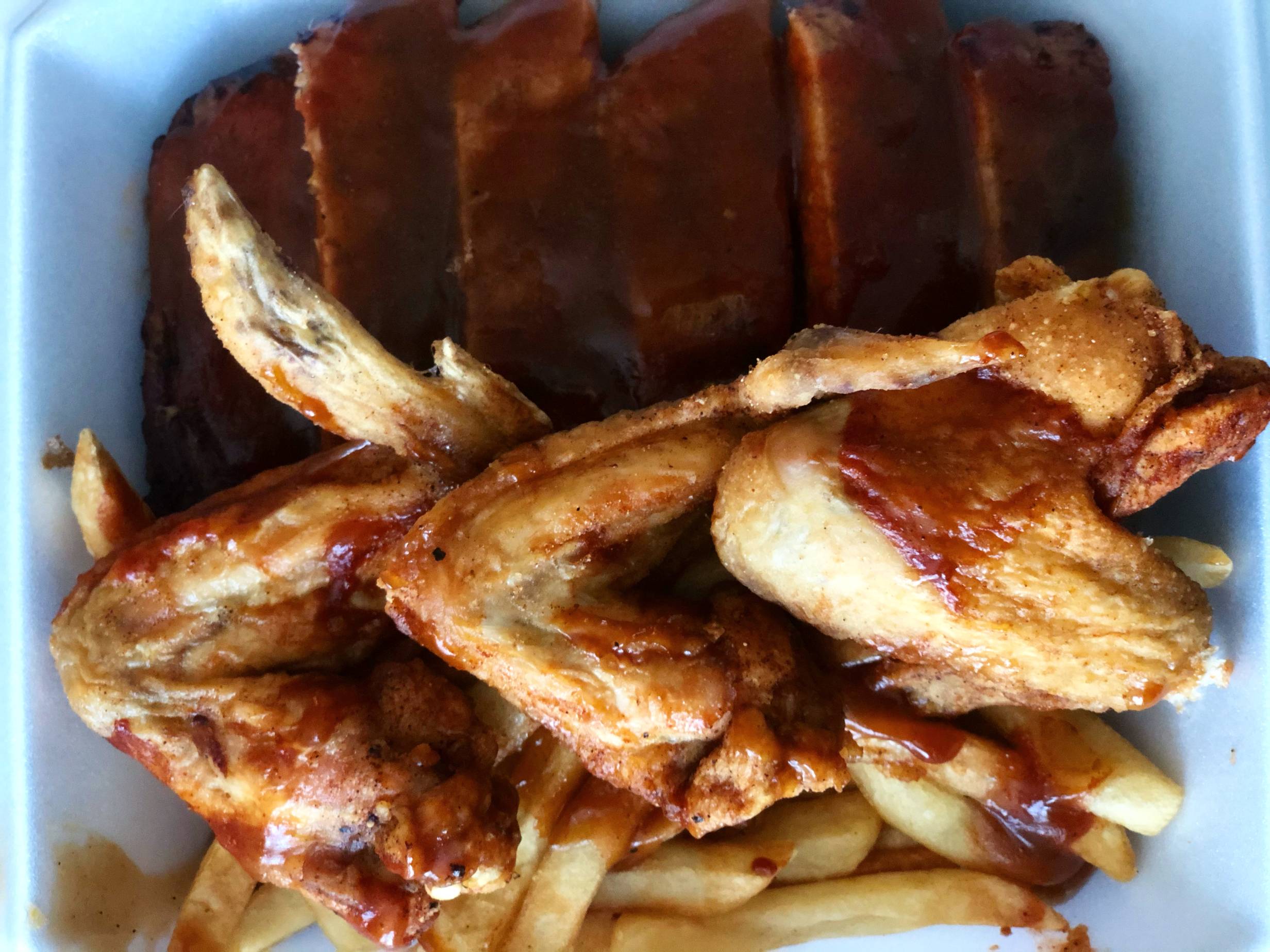 Three large wings lightly sauced sit on top of french fries in a styrofoam container next to ribs with sauce. Photo by Alyssa Buckley.