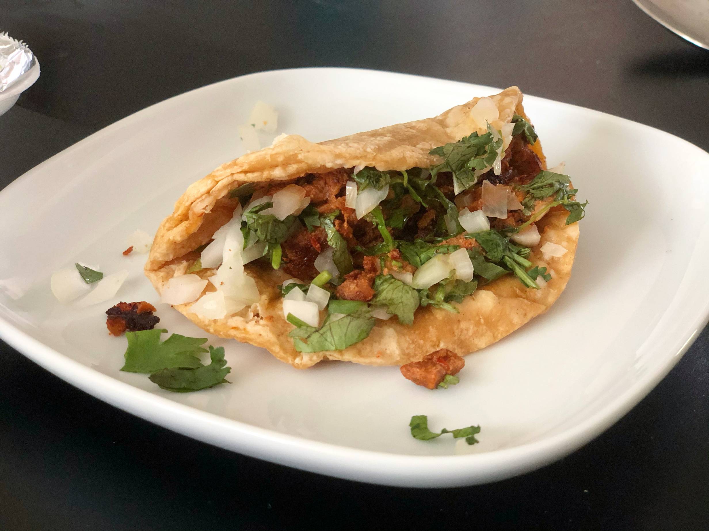 A pastor taco on a corn tortilla is overflowing with pork, cilantro, and onions on a white plate. Photo by Alyssa Buckley.
