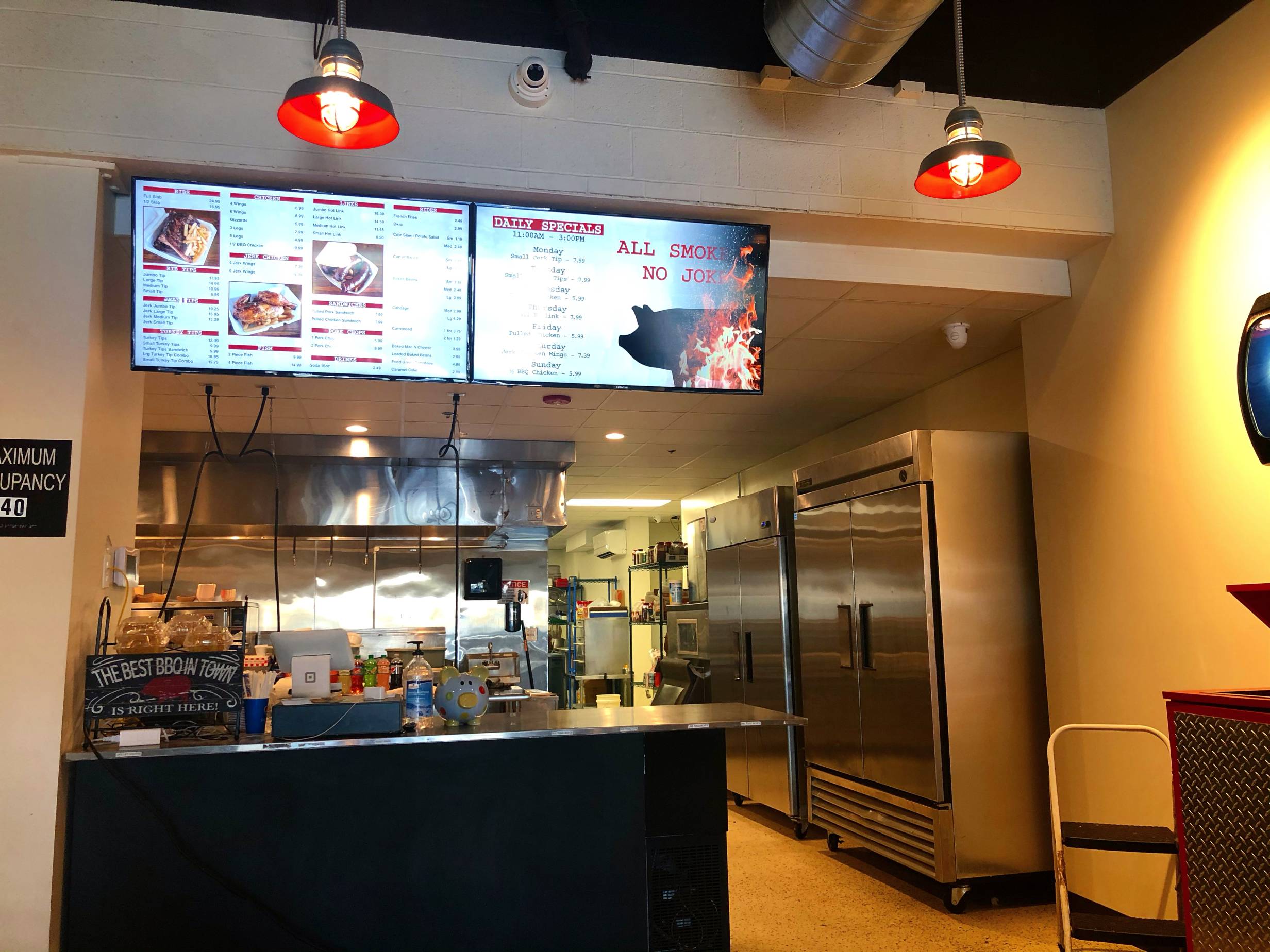 The counter inside Wood N' Hog's Champaign restaurant. A menu is hanging high above, and there are many stainless steel kitchen appliances visible. Photo by Alyssa Buckley.