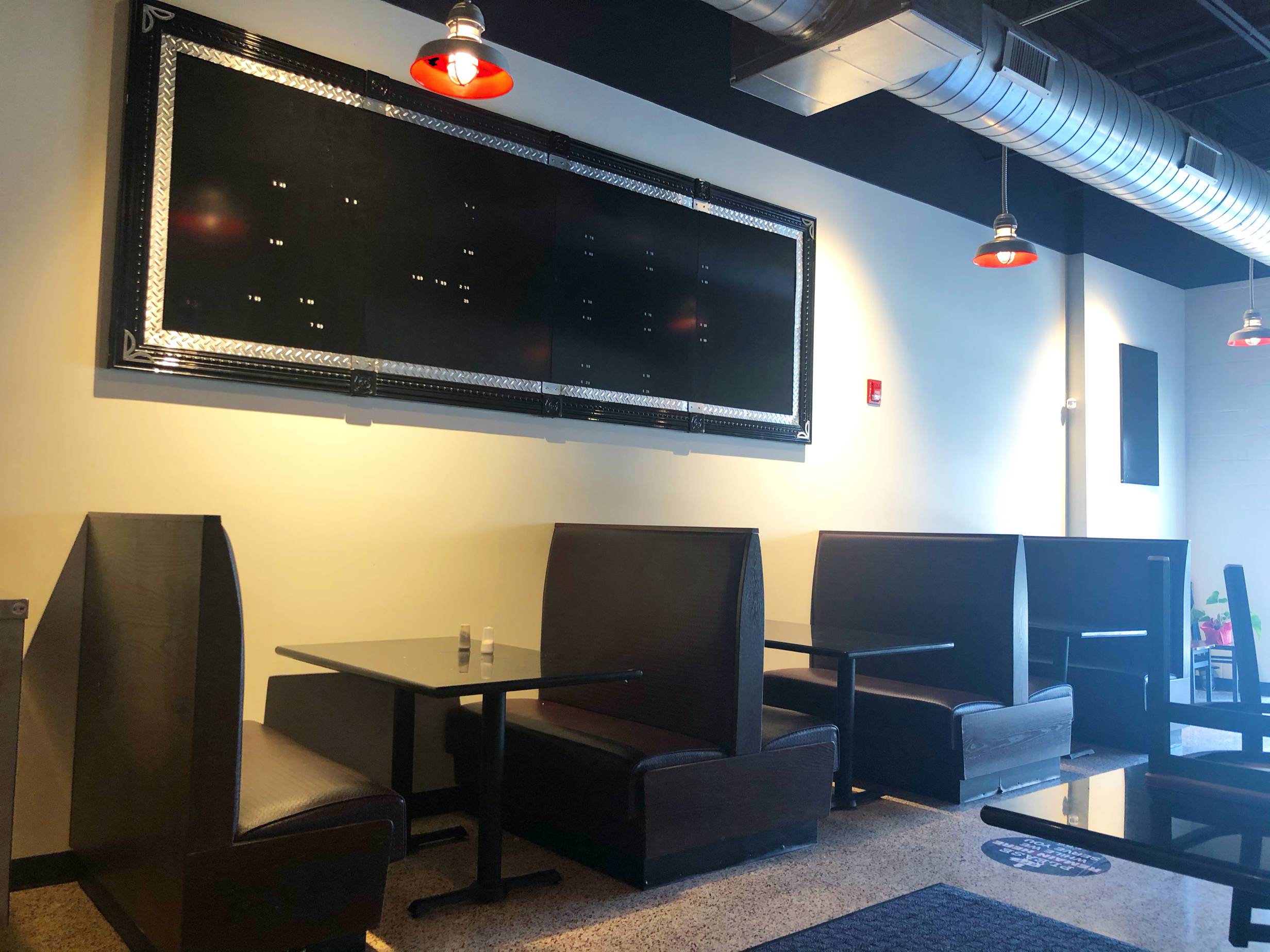 The interior of Wood N' Hog's Champaign location features several tall black booths with simple tables. There is artwork above that is long and rectangular with a black background and a few yellow smudges. Photo by Alyssa Buckley.