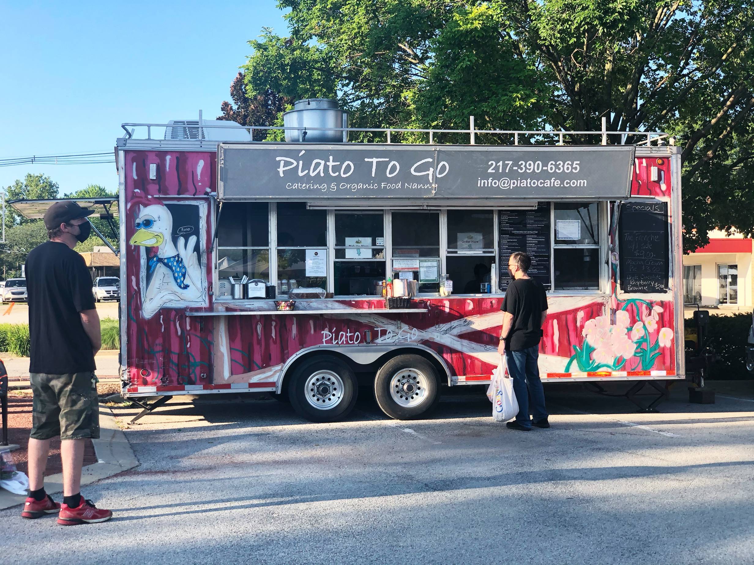 A red food truck with a sunglasses-wearig chicken, Piato To Go is parked in a parking lot while two customers wait to be served. Photo by Alyssa Buckley.