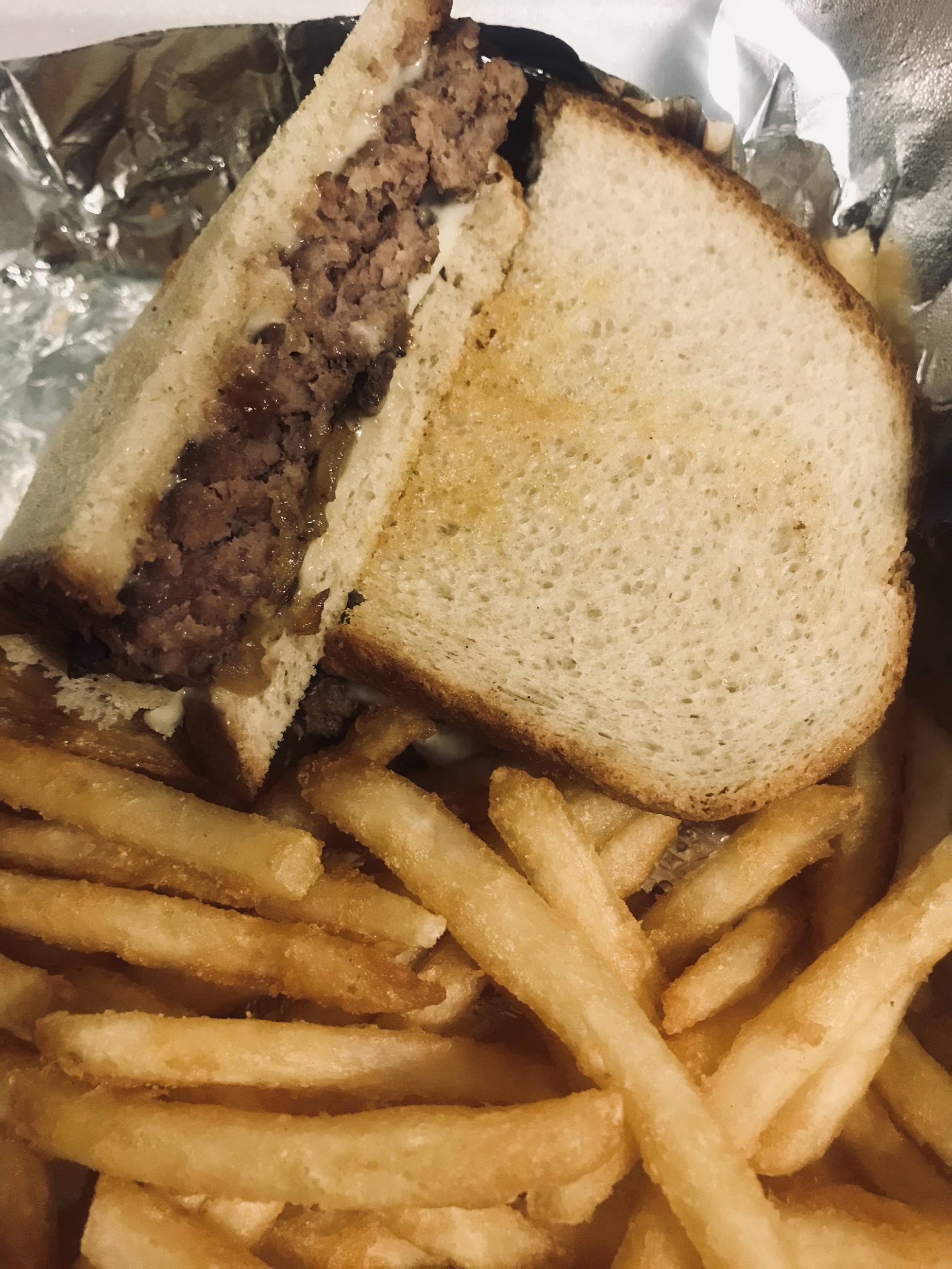 Patty Melt at Goldyâ€™s Bar and Grill. One half overlaps the other and inside a layer of burger, cheese, and grilled onion over a bed of seasoned, golden fries on a sheet of  aluminum foil in a styrofoam to-go box. Photo by Kanea Hughes.